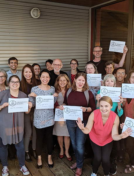 A group of people hold up #votescience campaign signs stating why they vote with science and evidence in mind