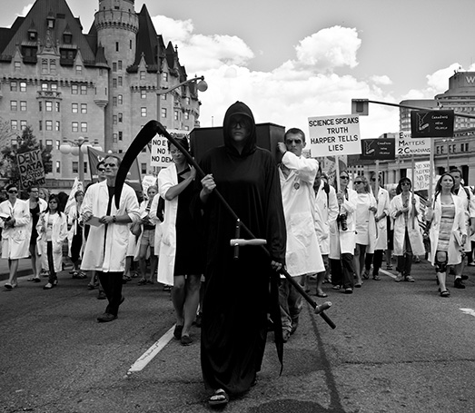 A person dressed up as the Grim Reaper leads a procession of protestors dressed in lab coats during the Death of Evidence rally protest