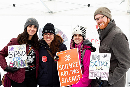 Four people stand with signs from the Vote Science campaign